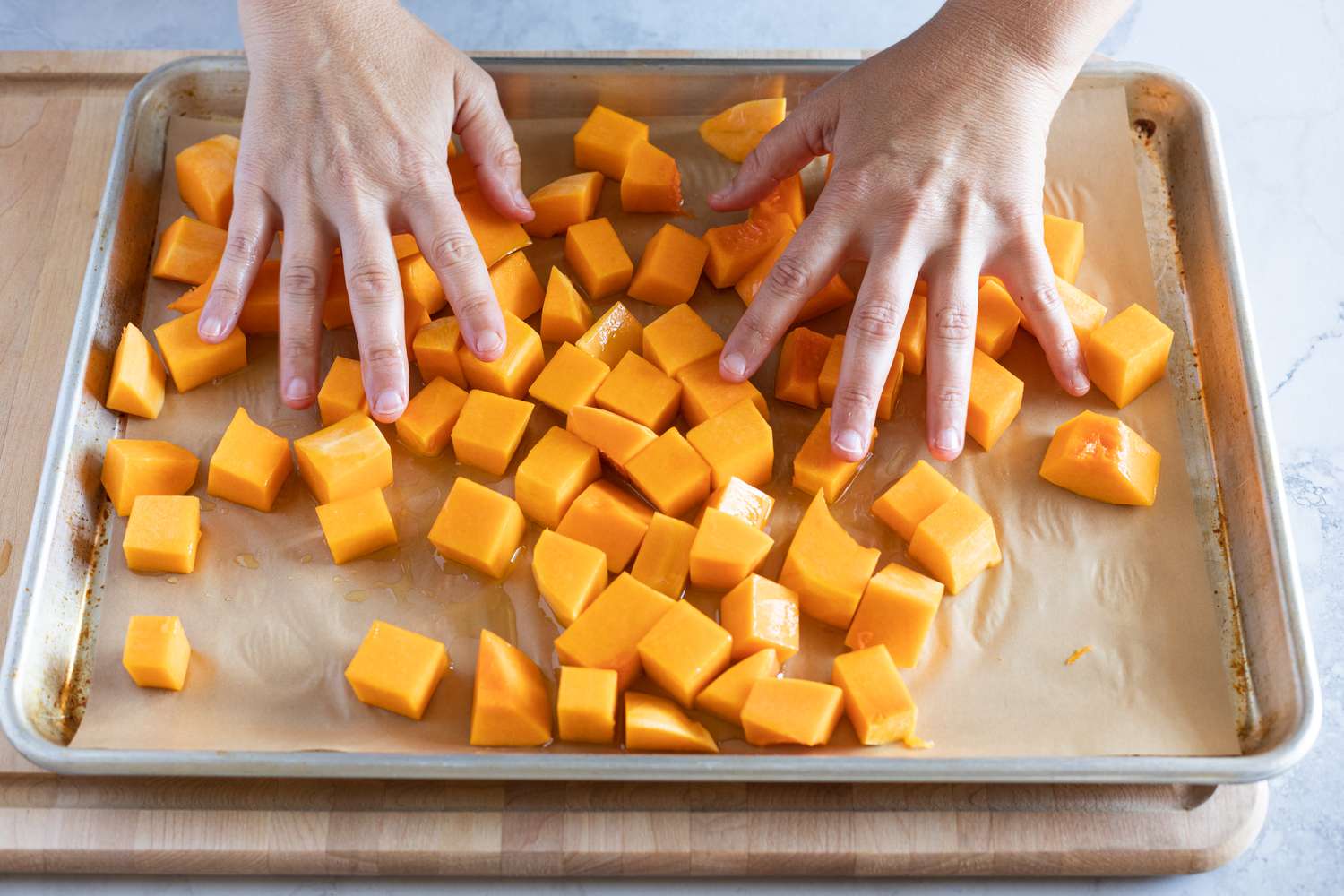Hands coating butternut squash with olive oil
