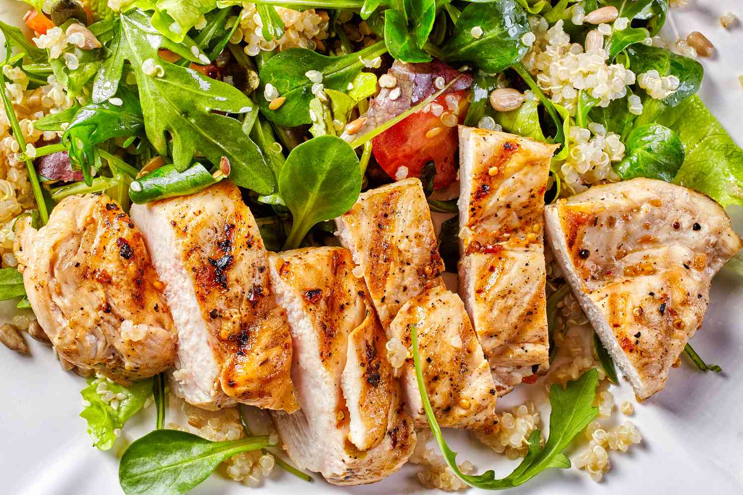 Sliced grilled chicken breast on a bed of greens and quinoa salad