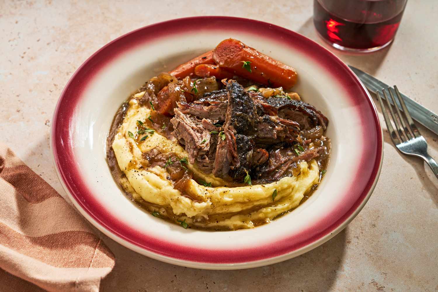 A serving bowl of pot roast over mashed potatoes with carrots on the side