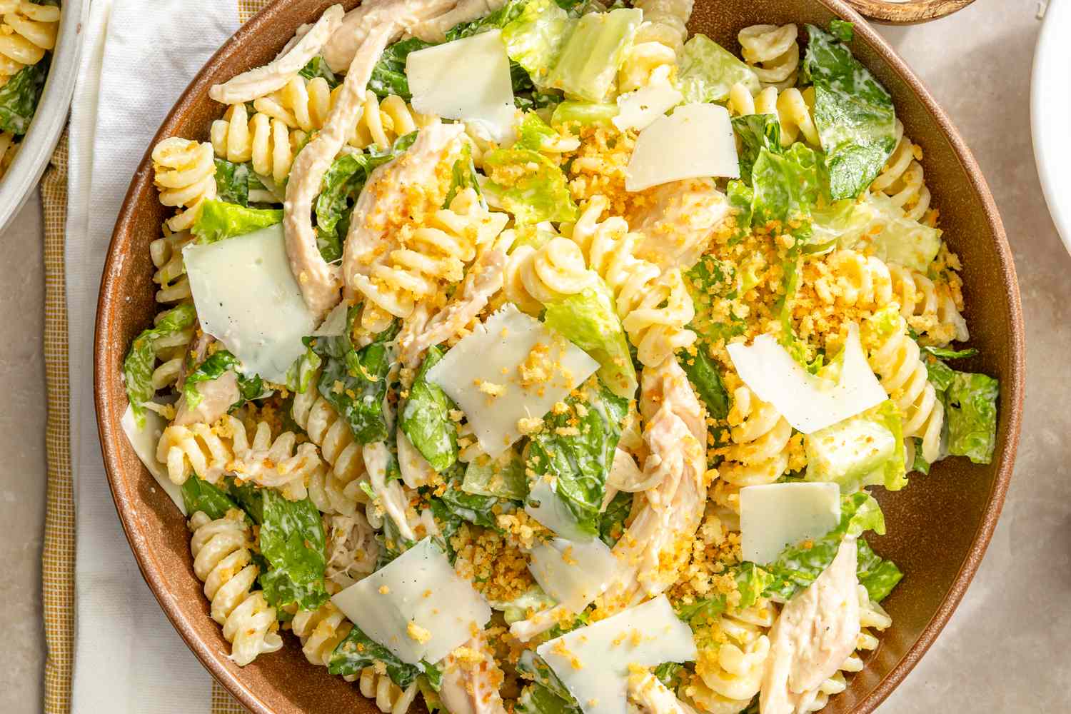 Chicken Caesar pasta salad with shredded chicken, romaine lettuce, fusilli pasta, Parmesan cheese, and crouton crumbs in a bowl