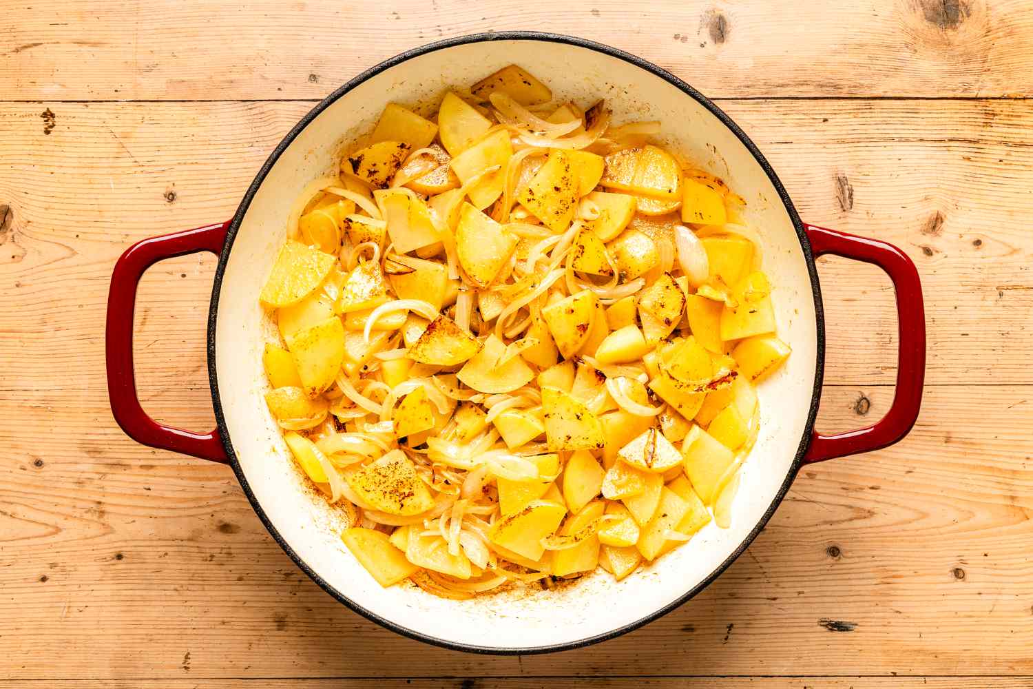 Overhead view of a red and white cast iron skillet with potatoes and onions for Kielbasa, Potato, and Broccoli Skillet recipe