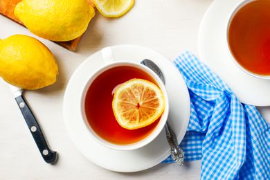 Cup of tea with a slice of lemon at a table setting with another glass of tea and lemons