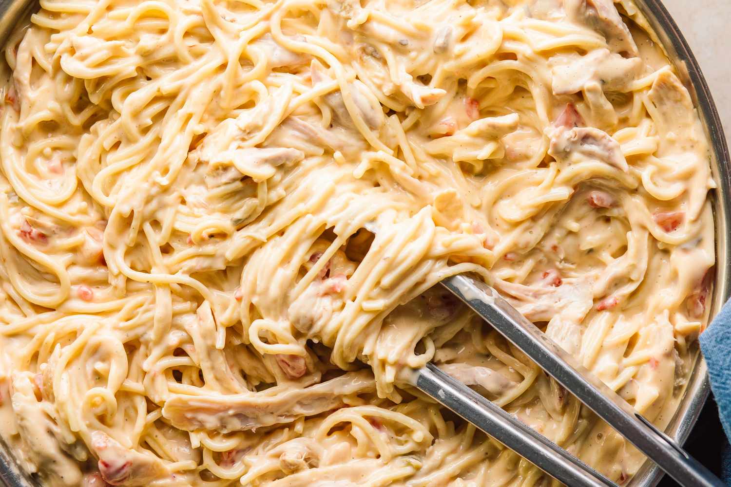 close up view of Chicken Queso Spaghetti in a pan with tongs