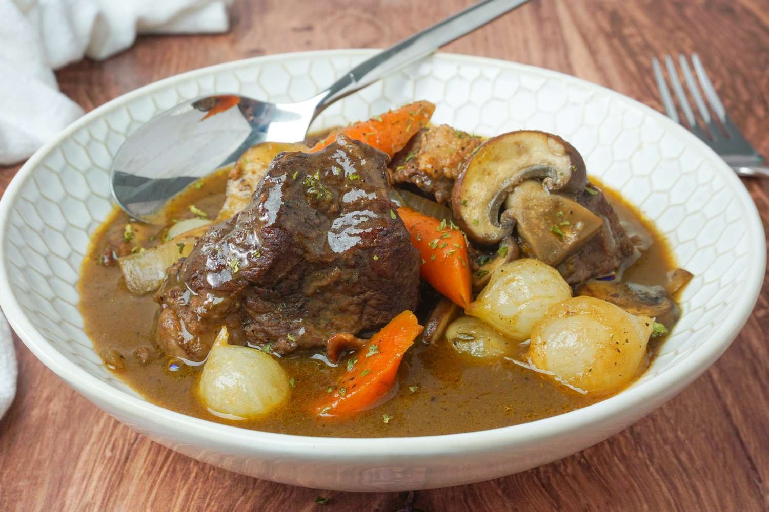 A bowl of beef bourguignon with carrots mushrooms onions and sauce served with a spoon