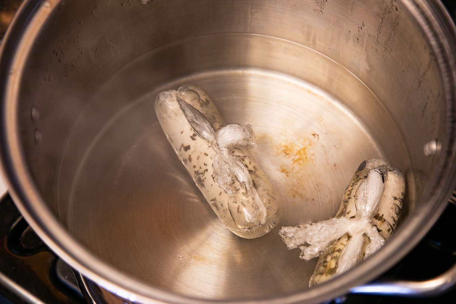 Plastic wrapped chicken in a large pot of water to make a poached chicken recipe.