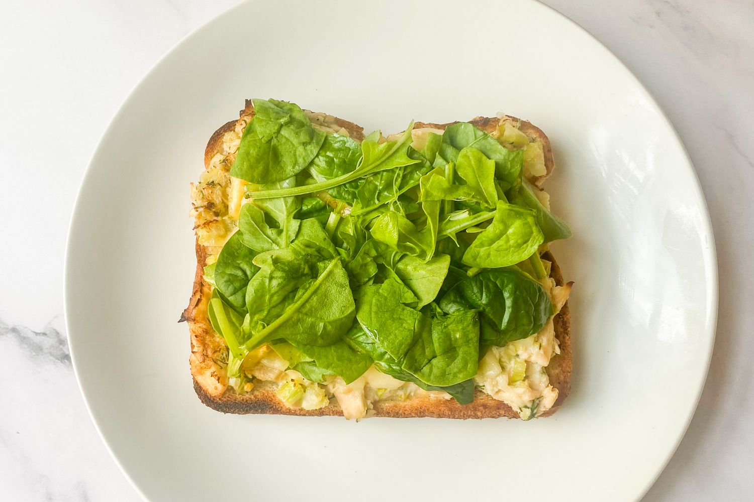 An open-faced tuna melt on toast topped with spinach