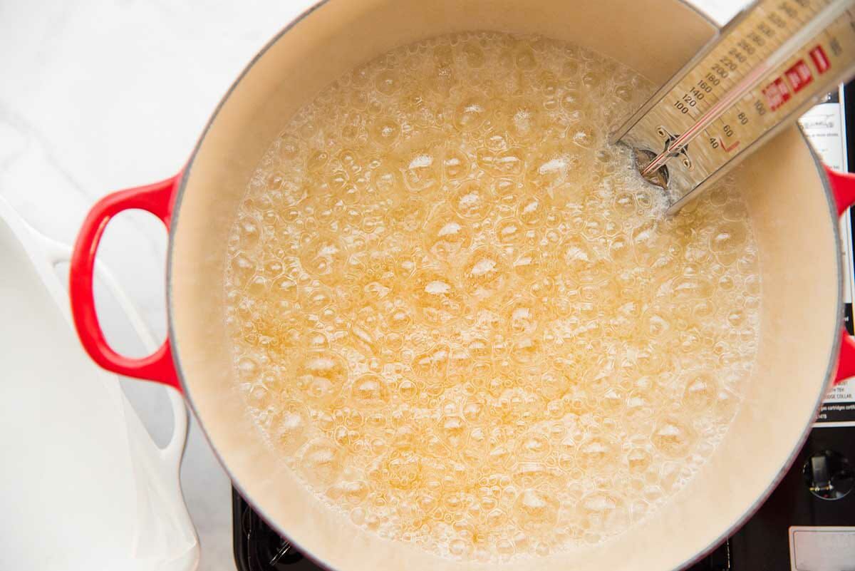 A candy thermometer in a dutch oven with simmering sugar to make Homemade Caramel Candy.