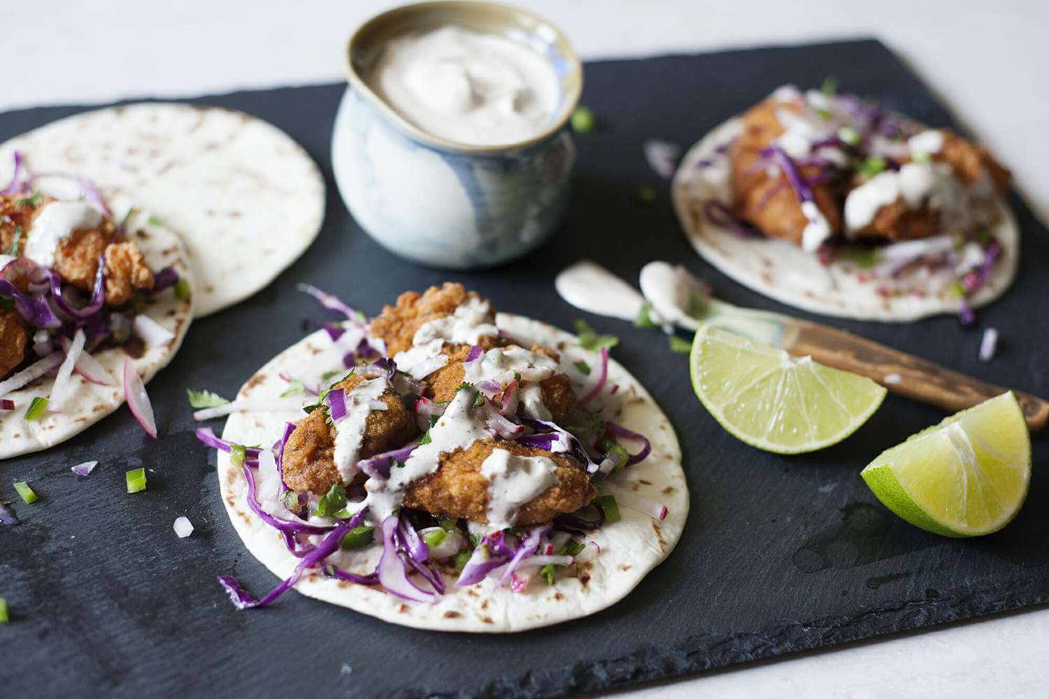 Best cod Tacos with slaw and crema - fish tacos on grey slate with crema and lime