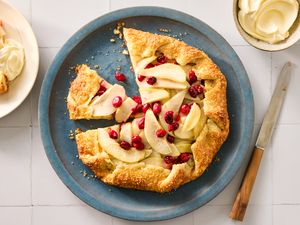 A pear and cranberry galette on a plate with a slice removed next to a serving of whipped cream
