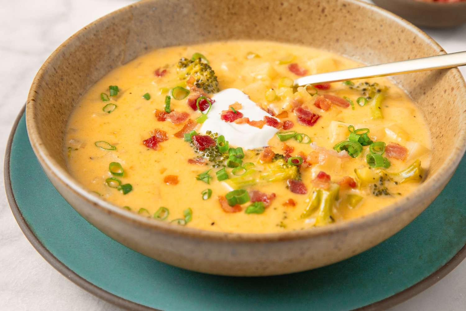 Broccoli potato soup in a bowl with garnishes of sour cream scallions and crumbled bacon