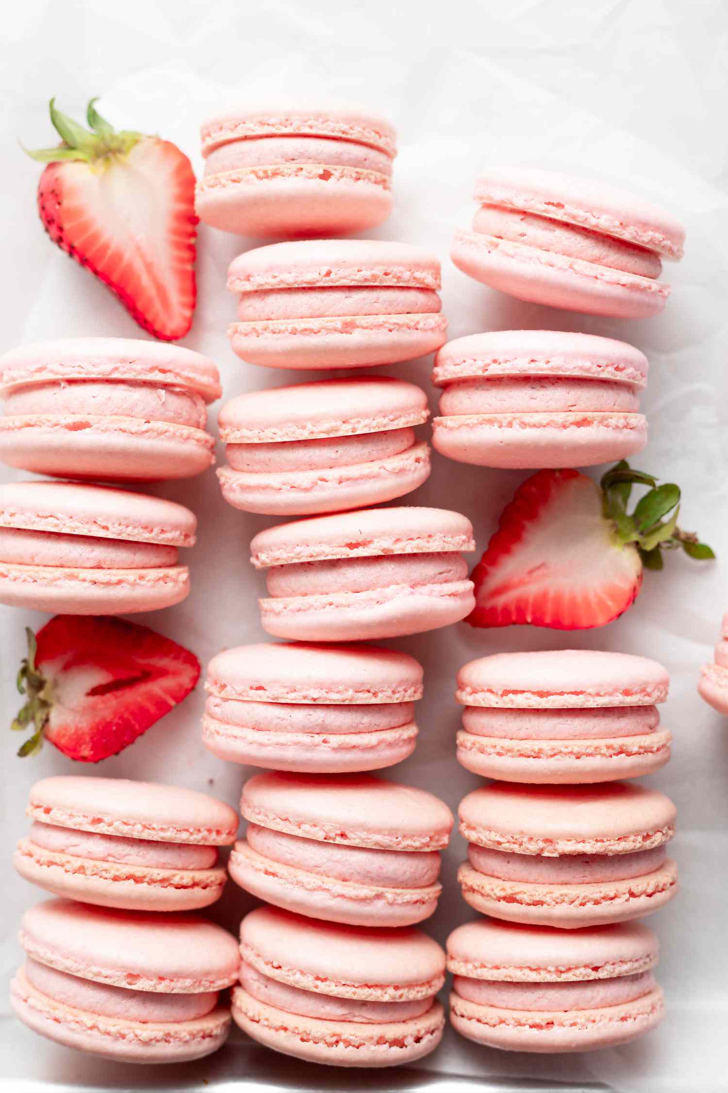 Overhead view of strawberry macarons lined up on their side with halved strawberries set in-between the rows.