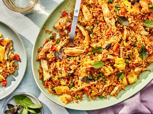 Thai-style fried rice on a platter at a table setting with a serving of fried rice on a plate, a small plate with Thai basil, a glass of water, and a table napkin