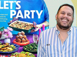 A person smiling in front of a cookbook titled Lets Party with a spread of food on the cover