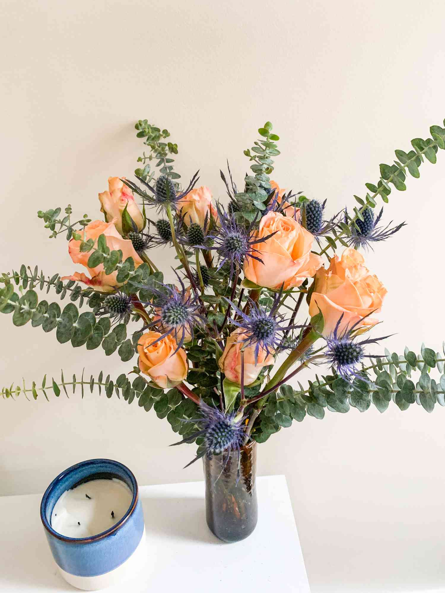 Bouquet of Flowers and Eucalyptus in a Vase on a Table Next to a Candle