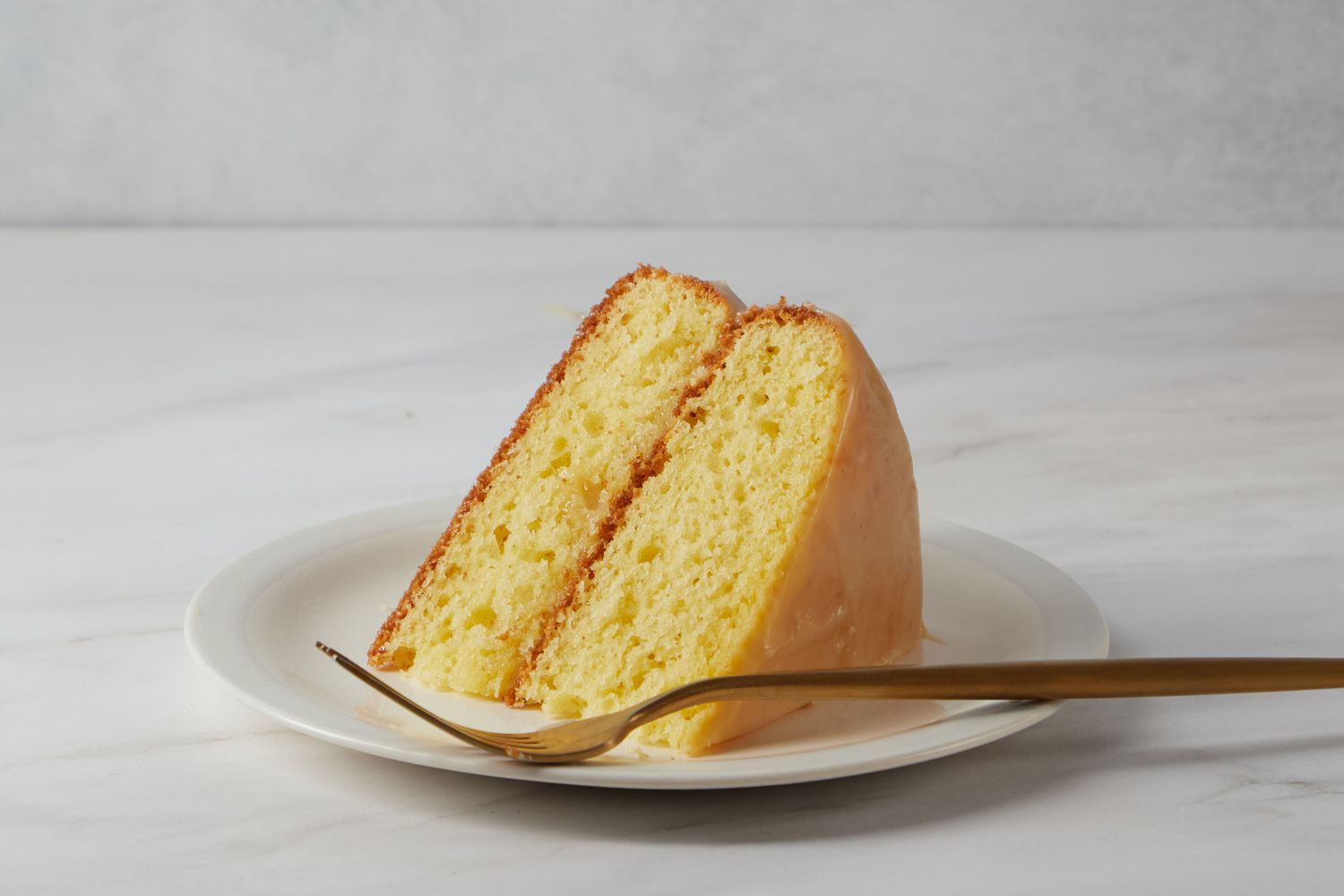 Two slices of layered cake on a plate with a fork featuring a creamy glaze or filling for Reese Witherspoon's Sour Cream Cake