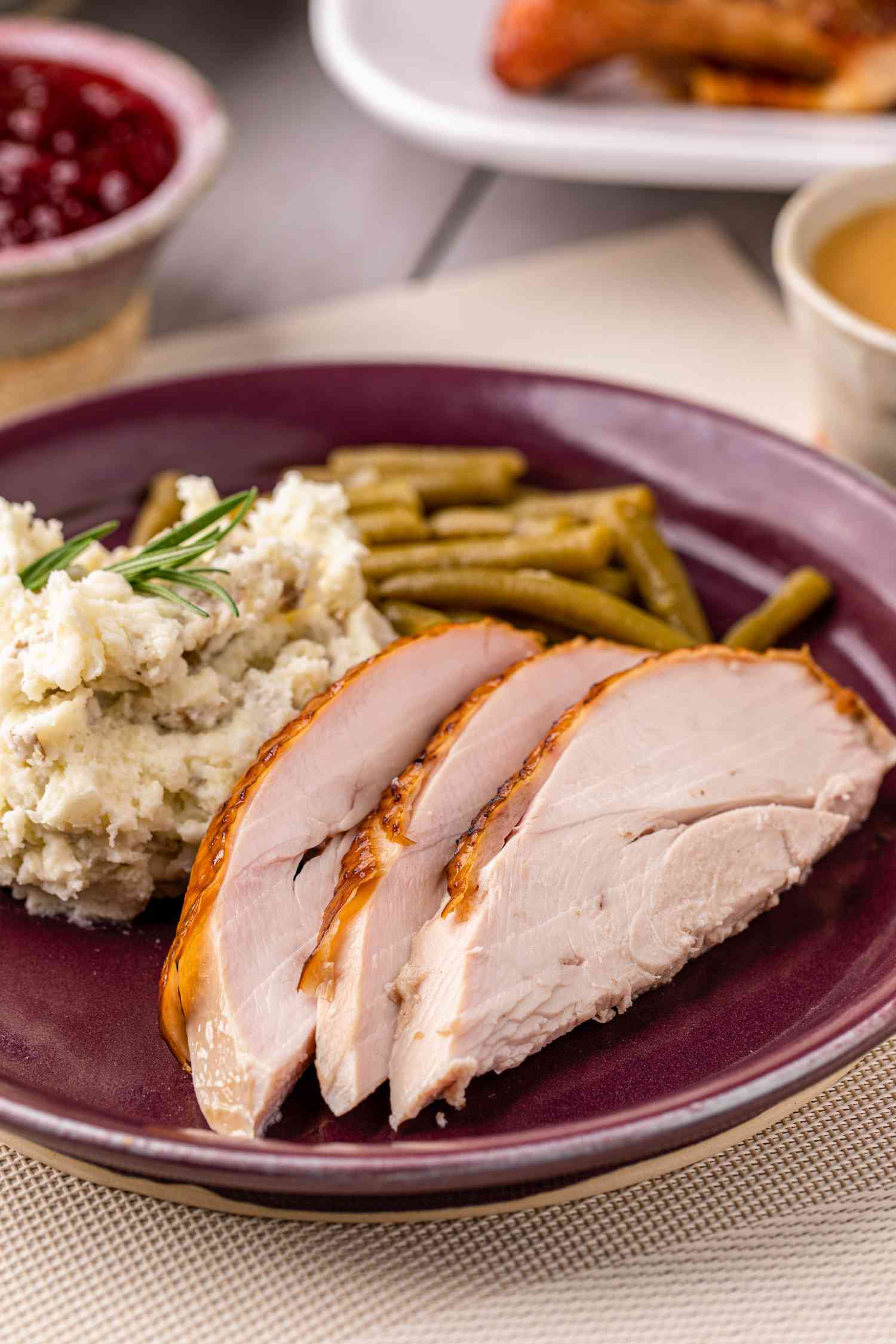 Pecan wood smoked turkey sliced on a plate next to green beans and mashed potatoes.