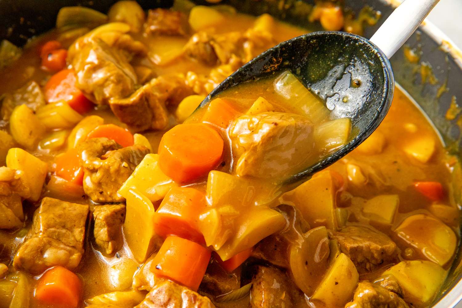 A spoon of Japanese curry with vegetables and meat being served from a pan