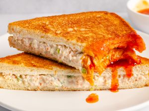 Grilled sandwich filled with a creamy crab mixture served on a white plate with a sweet and sour dipping sauce
