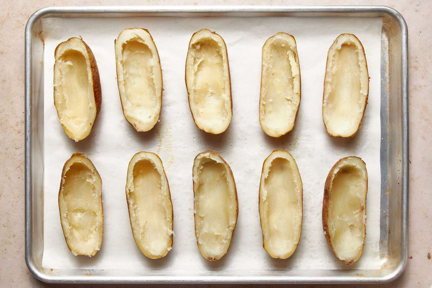 Baked potato shells on the parchment paper-lined baking sheet for twice baked potatoes recipe