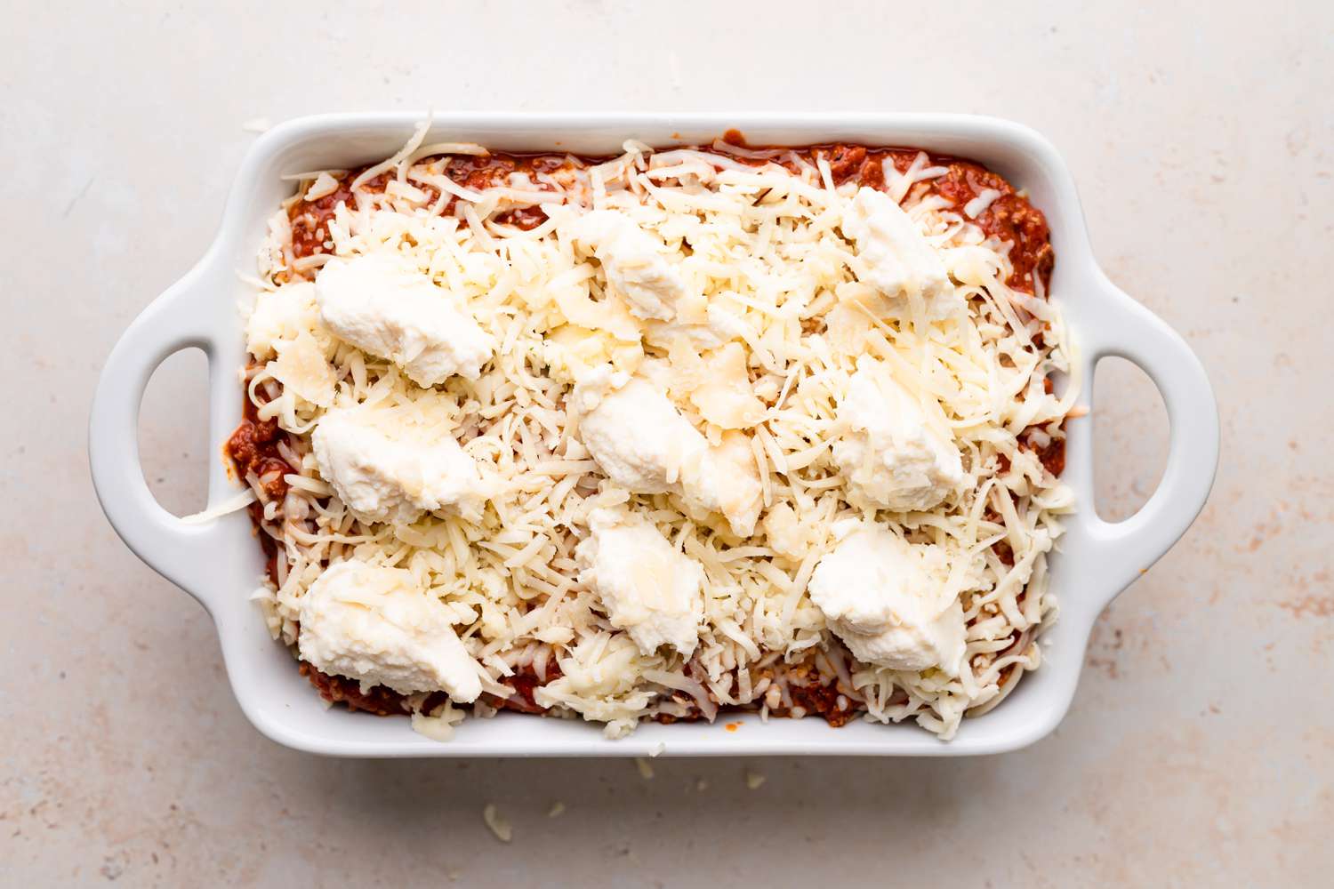 Topping meat sauce with shredded cheese and ricotta to make the best lasagna recipe.