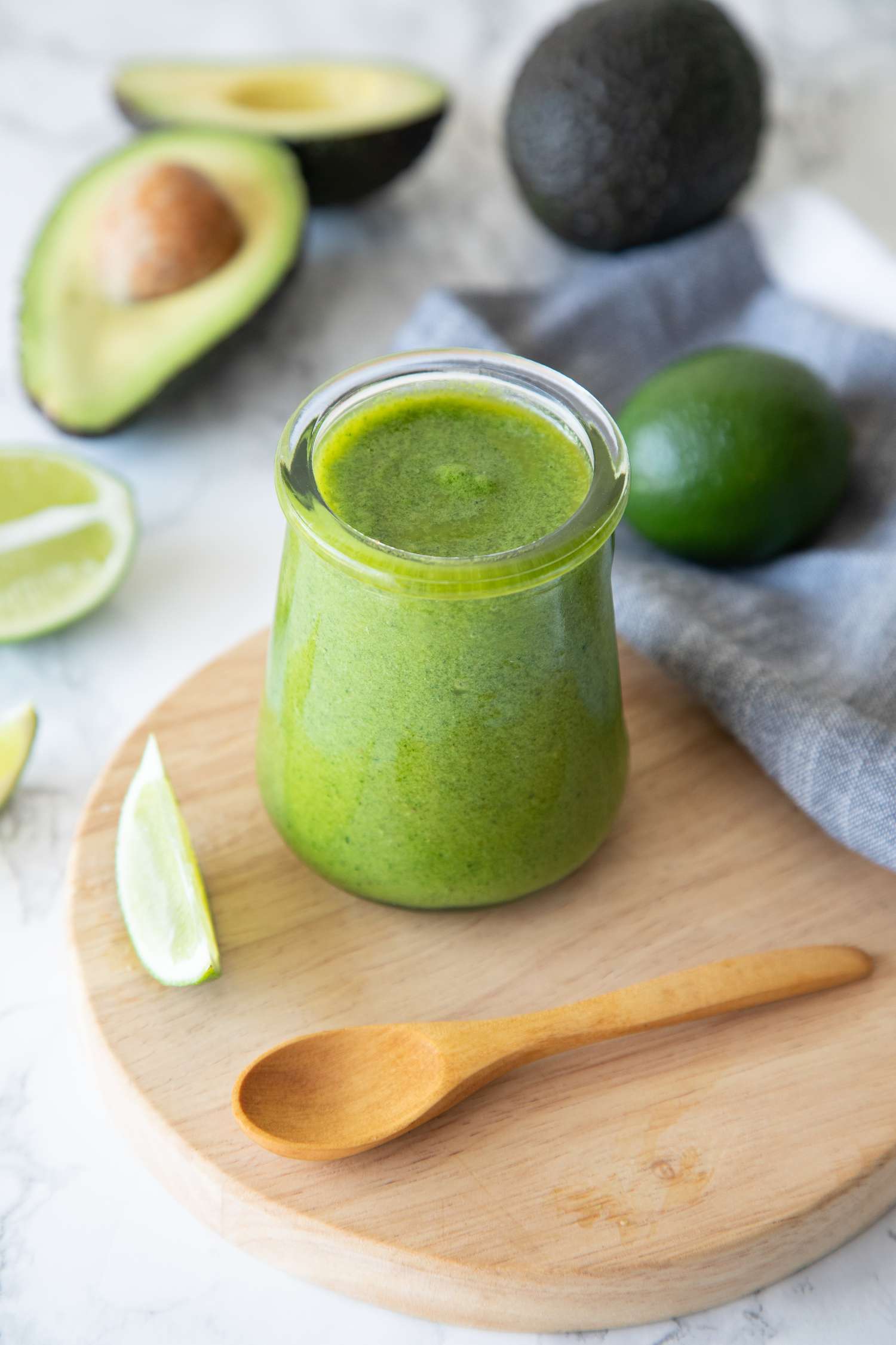 Jar of Avocado Lime Dressing on a Wood Tray Next to Limes, Avocados, and a Spoon