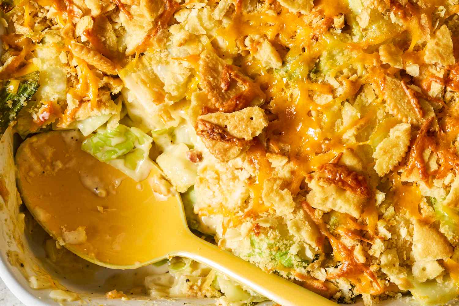 A serving of baked cabbage casserole with cheese and crispy toppings a yellow serving spoon in the dish