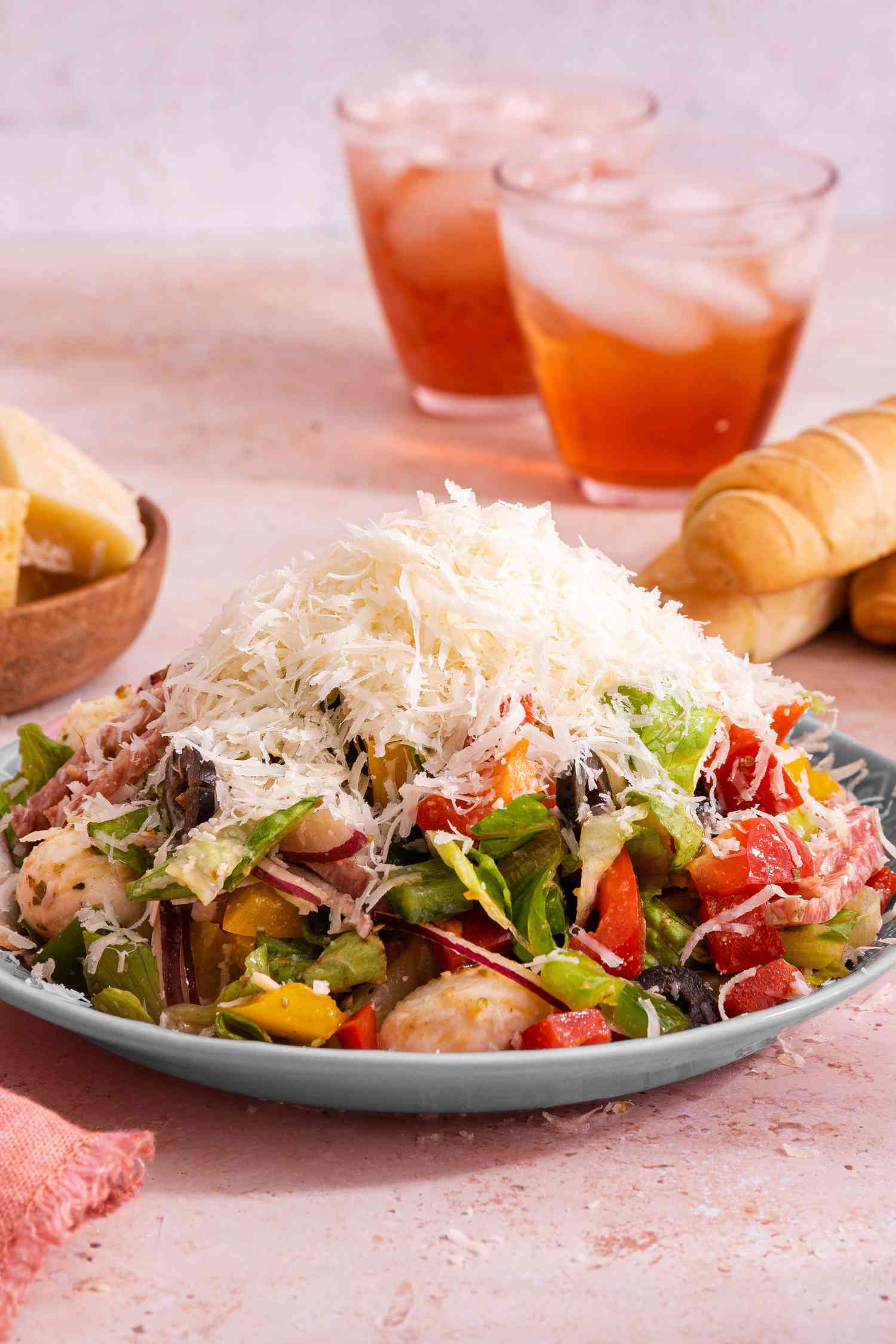 Plate of Pizza Salad Topped With Grated Parmesan, and in the Background, a Bowl With Small Parmesan Blocks, Breadsticks, and Two Iced Drinks