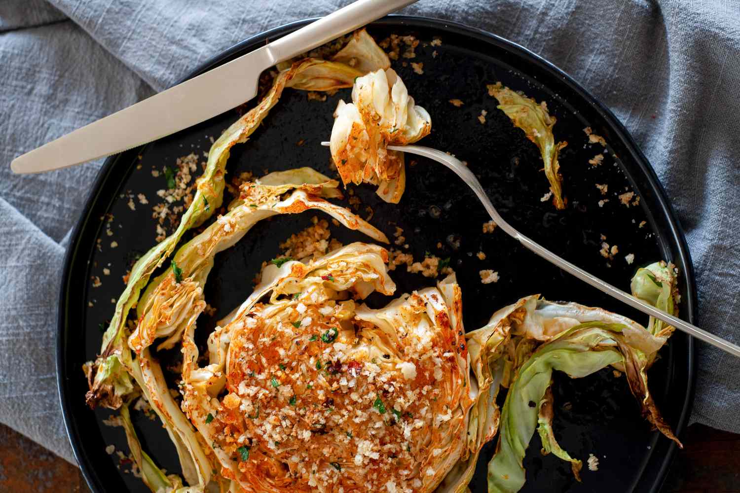 Forkful of crunchy garlic breadcrumbs over simply roasted cabbage on a black plate.