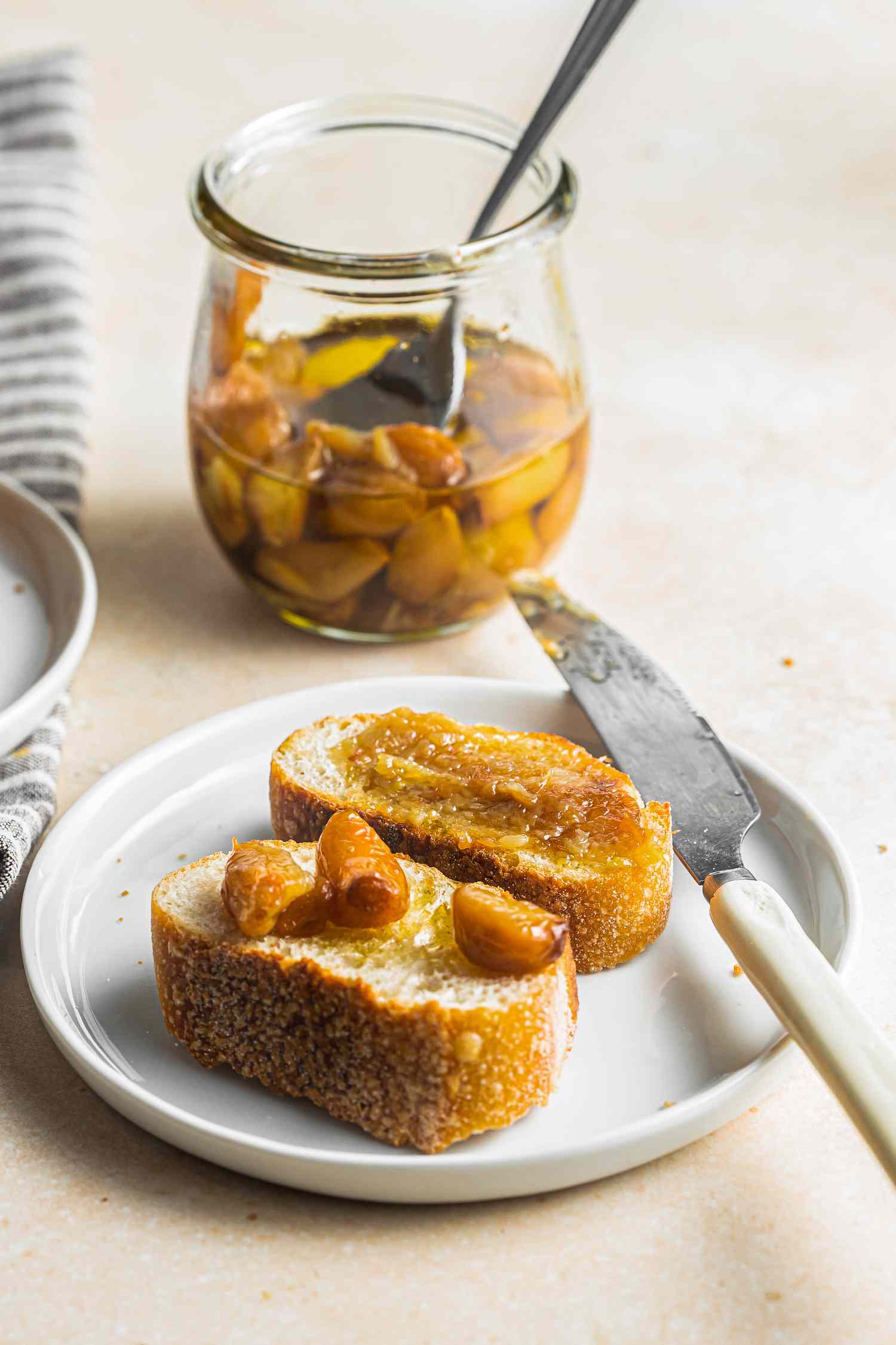 Toast with Garlic Confit on Plate with Butter Knife With Jar of Confit in Background 