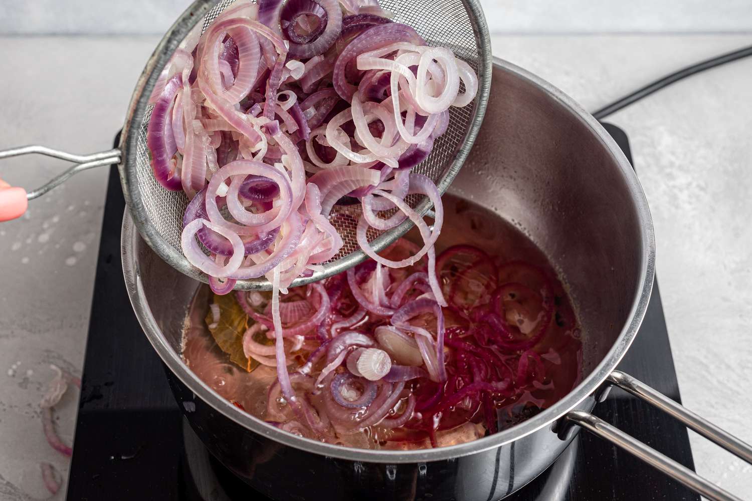 Adding blanched onions to vinegar and spices in a pot to make a pickled red onions recipe.