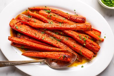 Dish of cooked carrots on a white plate with chopped herbs and a serving spoon
