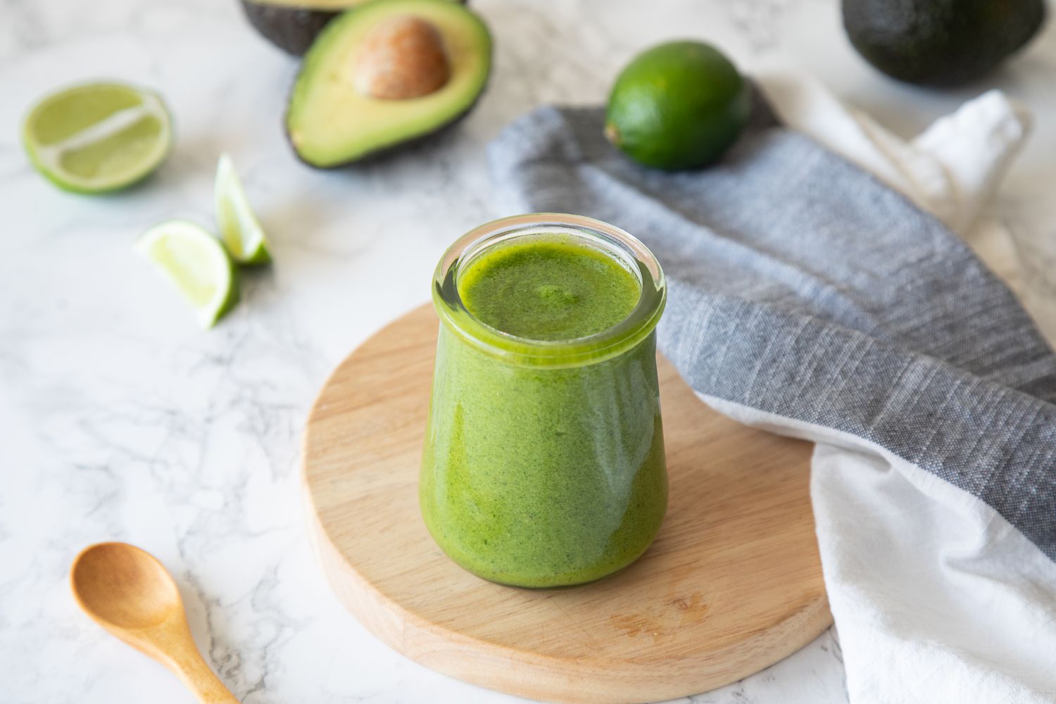 Avocado Lime Dressing on Wooden Tray Next to a Spoon, Limes, and Avocados