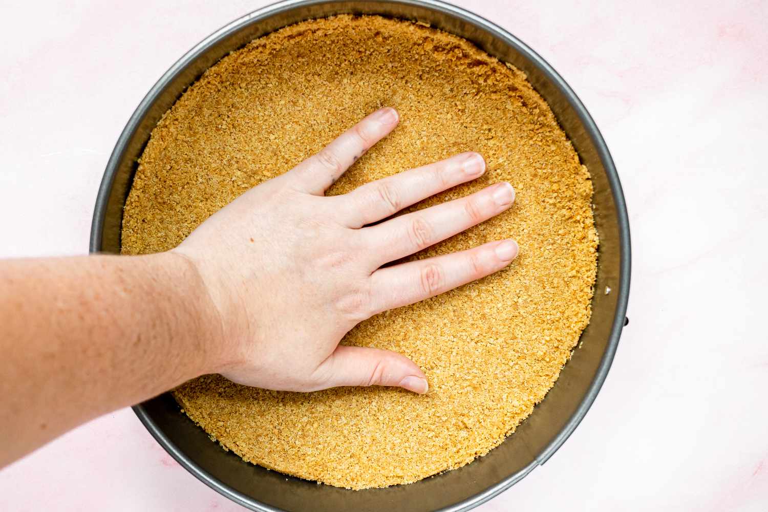 A hand pressing the graham crust into a springform pan