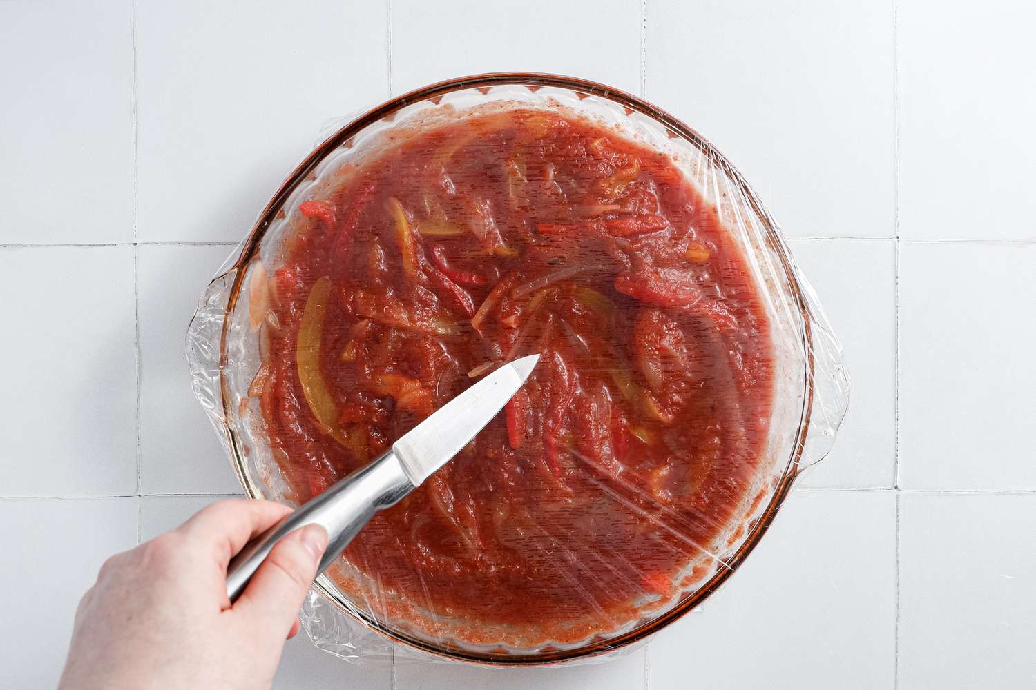 Glass Pyrex Dish Covered with Plastic Wrap and Pierced with a Knife for Microwave Shakshuka 
