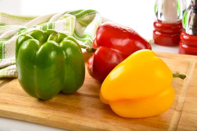 Red, green and yellow peppers on a cutting board