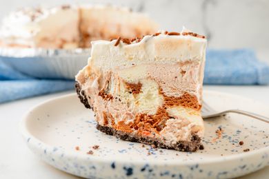 A slice of layered ice cream pie on a speckled plate with a fork