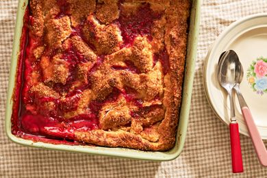 peach and raspberry pandowdy in a casserole dish next to a stack of plates on comfy (cottage-core style) table 