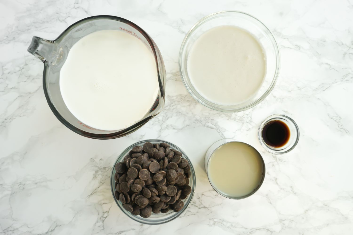 Ingredients for a hot chocolate recipe including milk cream chocolate chips sweetened condensed milk and vanilla extract on a counter