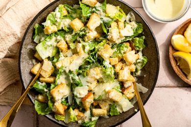 Caesar salad with croutons and Parmesan in a bowl with dressing and lemon on the side
