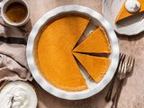 Overhead shot of no-bake pumpkin pie in a pie dish at a rustic setting with a cup of coffe, a grey-ish beige table linen, bowl of whipped cream, and a plate with a slice of pumpkin pie with a dollop of whipped cream