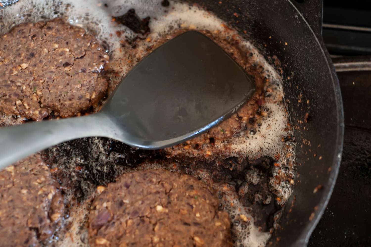 Black Bean Burger Patty Smashed Down Using a Spatula While It Continues to Cook in the Cast Iron Skillet