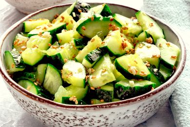 A bowl of sliced cucumbers mixed with sesame seeds, placed on a light-colored surface