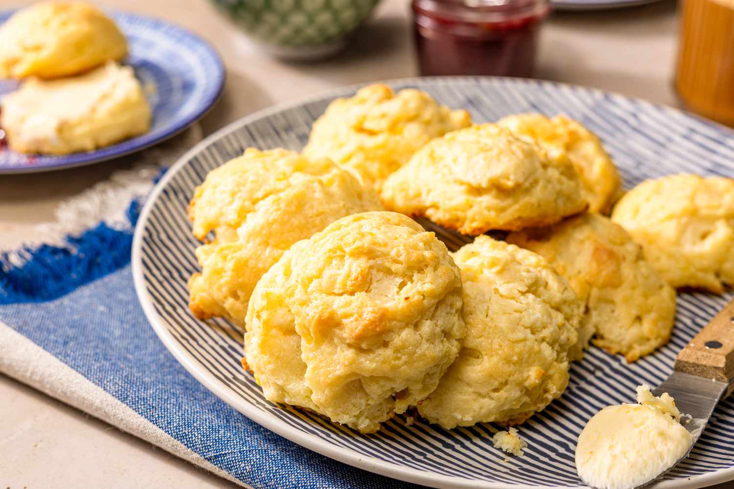 Angled view of a plate of mashed potato biscuits ready to serve next to a plate with one sliced biscuit with butter