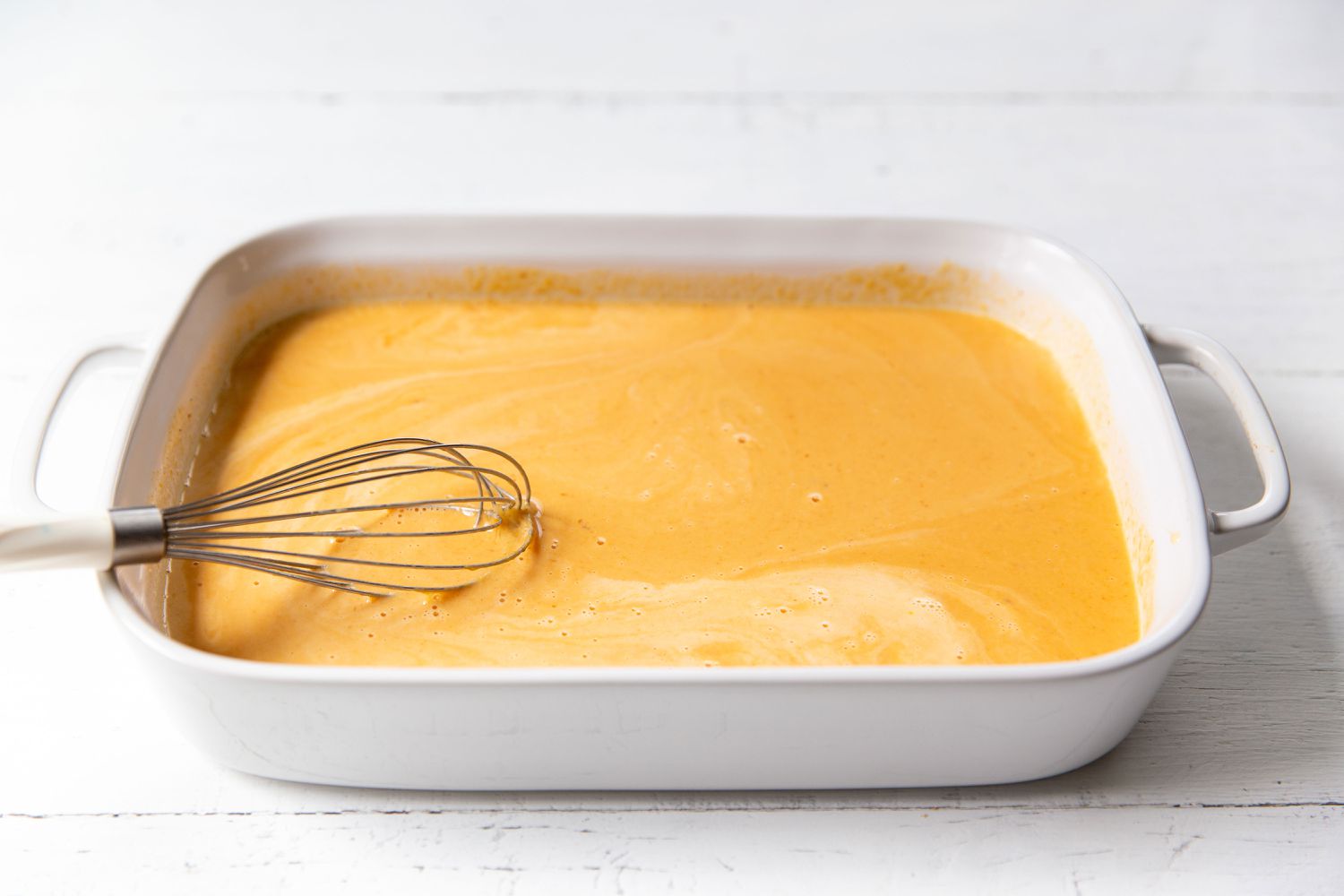 ingredients in baking dish mixed together with a whisk for Pumpkin Dump Cake