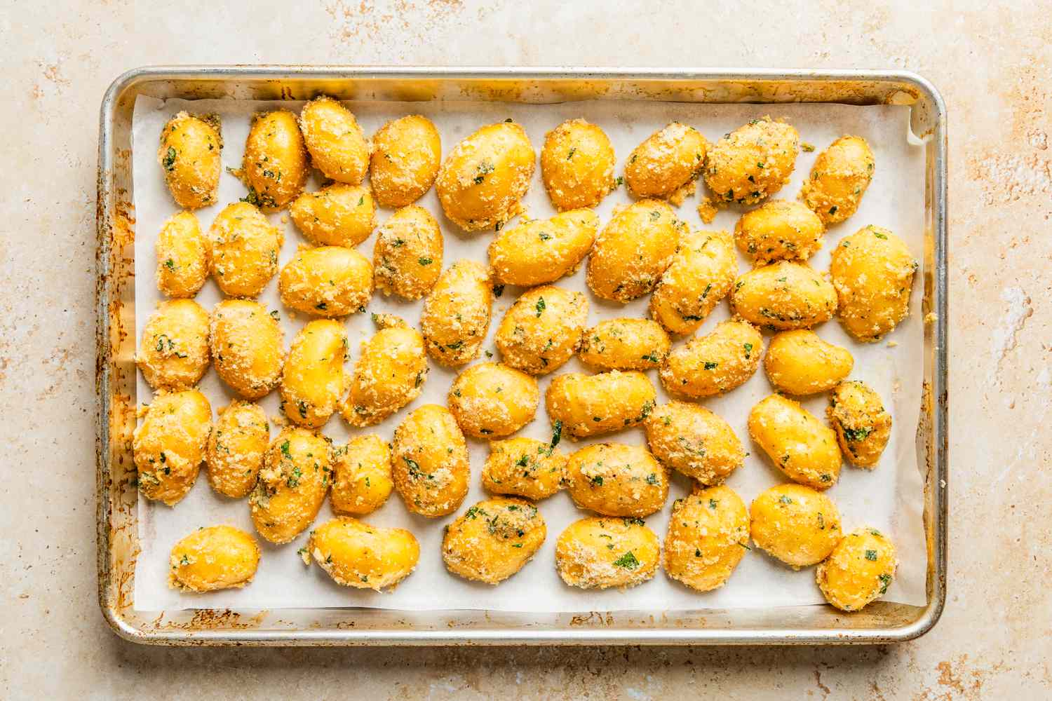 parmesan potatoes added to a parchment-paper lined baking sheet for crispy parmesan potatoes recipe