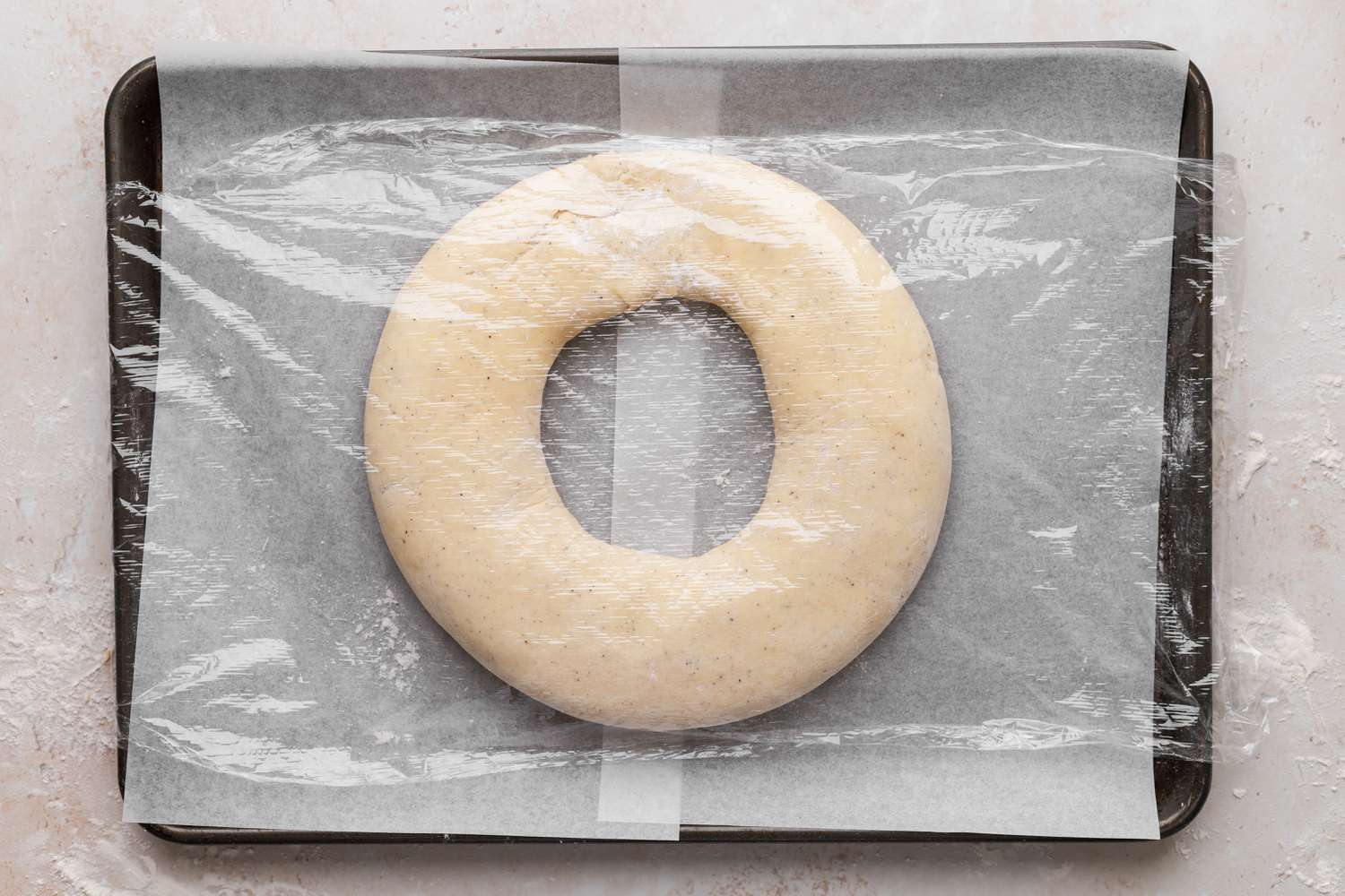 Kringle covered in plastic wrap on a baking sheet.