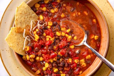 A bowl of chili with black beans corn diced tomatoes tortilla chips and a spoon