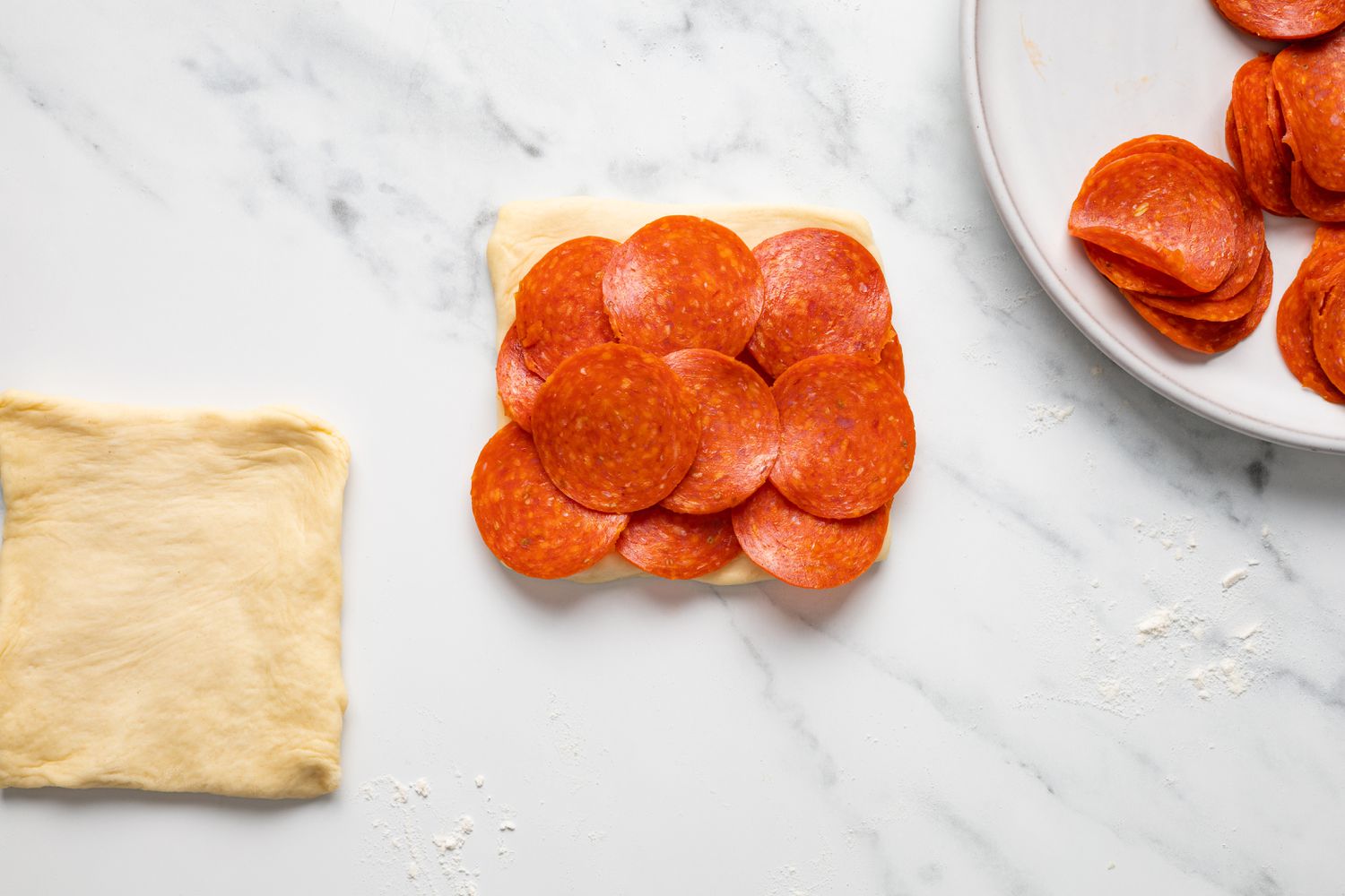 Pepperoni Added to Piece of Dough Next to More Dough and Pepperoni 