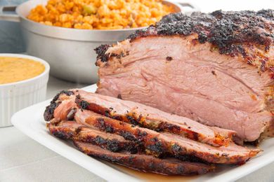 Caramelized mojo marinated pork roast with four juicy slices cut from it. A small white bowl of marinade rests next to a larger bowl of red rice.