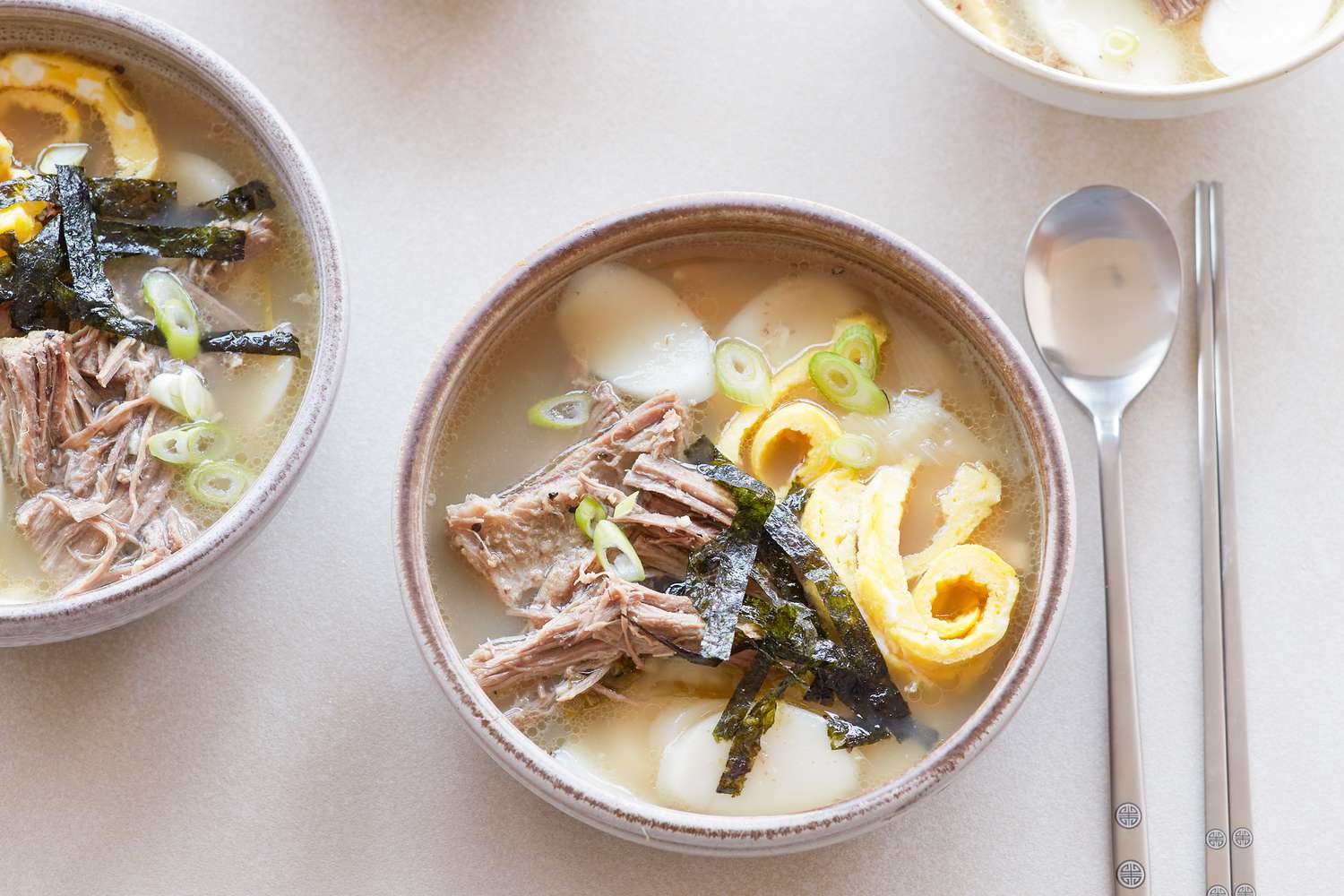 Overhead view of Korean rice cake soup on a table with a spoon.